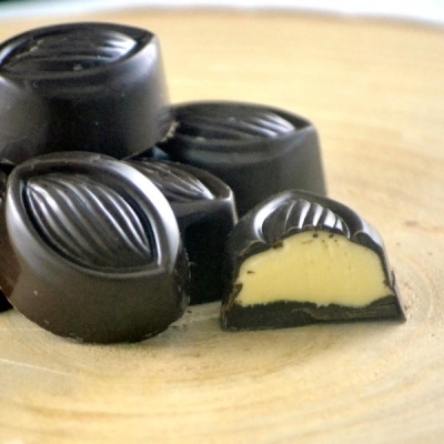 Bombons de chocolate preto com recheio cremoso amarelo e padrão ondulado no topo