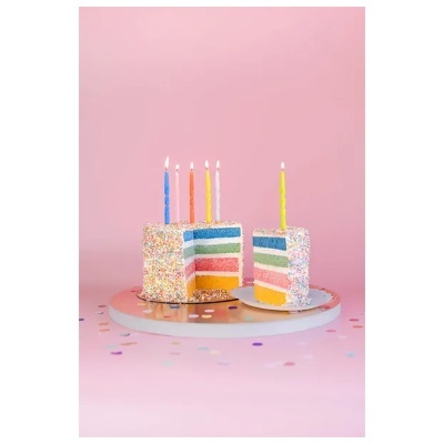 Bolo de aniversário colorido com velas acesas e confetis em fundo rosa