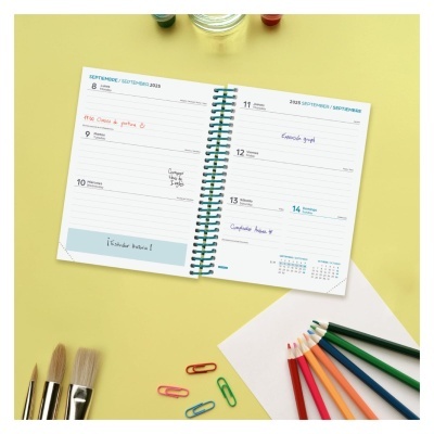 Agenda semanal aberta com notas coloridas, pincéis, clips, lápis de cor e papel branco em fundo amarelo.