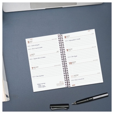 Agenda aberta numa superfície azul com caneta preta e portátil cinzento