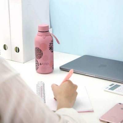 Garrafa térmica rosa com padrão de folhas pretas e texto AURA em mesa de escritório com portátil e outros objetos