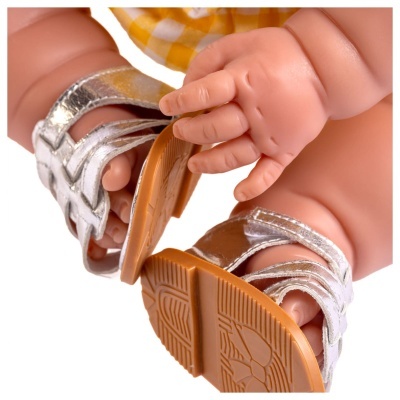 Pés de boneca com sandálias prateadas e roupa amarela xadrez.