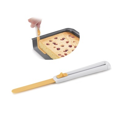 Espátula silicone amarela com cabo branco usada para cortar bolo numa forma preta.