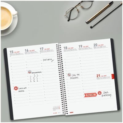 Agenda semanal aberta a 15-21 de março de 2027 com anotações, óculos, caneta, lápis e chávena de café numa mesa cinzenta.