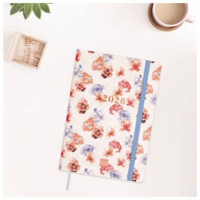Agenda 2026 floral com elástico azul sobre mesa branca com caneca e vaso