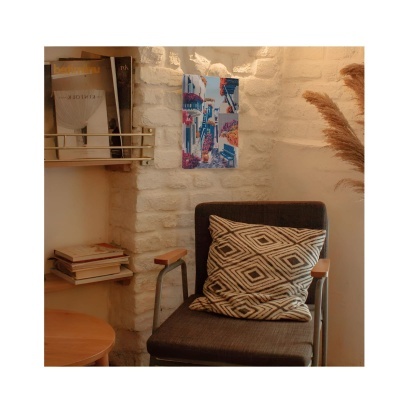 Cadeira com almofada padrão geométrico, parede de pedra branca com quadro colorido e prateleiras com livros