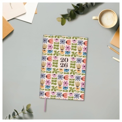 Agenda 2026 com capa floral colorida sobre mesa cinzenta com objetos de escritório