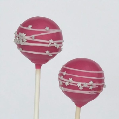 Dois cake pops cor de rosa com decoração branca em estrelas e linhas, em palitos brancos