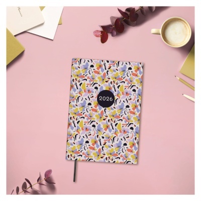 Agenda 2026 com capa colorida padrão abstrato sobre fundo cor-de-rosa