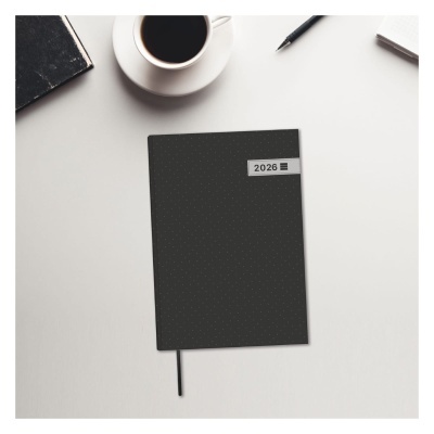 Caderno preto com inscrição '2026' sobre mesa branca com café e caneta