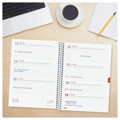 Agenda semanal aberta com datas e anotações, juntamente com teclado, chávena de chá, caderno e lápis sobre mesa de madeira clara