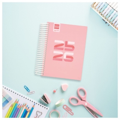 Caderno rosa com materiais de escritório organizados ao redor sobre fundo azul claro