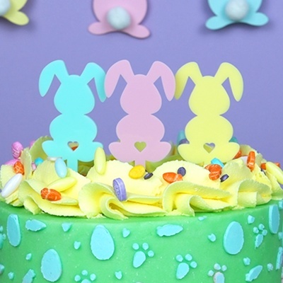 Bolo decorado com silhuetas de coelhos pastel no topo e na parede