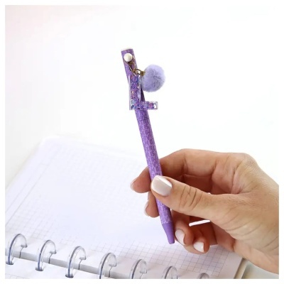 Caneta roxa com chaveiro letra e pompom sobre caderno quadriculado