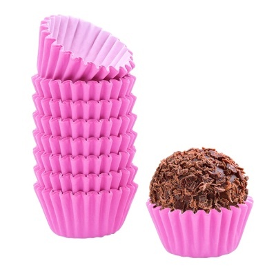 Papéis rosa para cupcakes empilhados à esquerda e brigadeiro com chocolate em forma rosa à direita