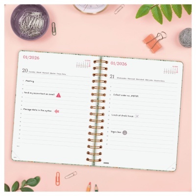 Agenda semanal aberta com capa verde claro e espiral dourado em fundo cor-de-rosa