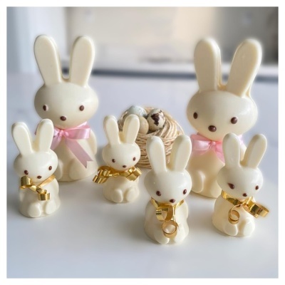 Seis coelhos decorativos em cerâmica branca com laços dourados e cor-de-rosa numa mesa