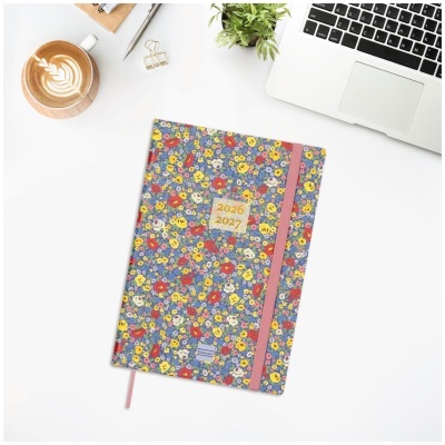 Agenda com capa floral 2026 2027, elástico rosa, sobre mesa branca com laptop, café, caneta e planta