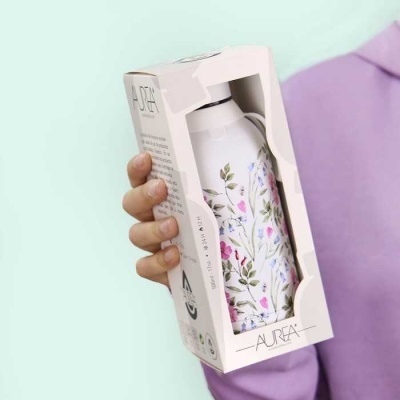 Garrafa isolada branca com padrão floral em embalagem de cartão branca sendo segurada por uma mão