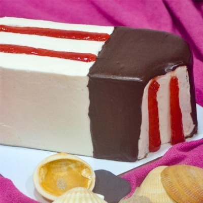 Bolo retangular com cobertura de chocolate e creme branco decorado com riscas vermelhas sobre pano cor de rosa e conchas