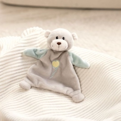 Pelúcia de ursinho cinzenta com braços azul-claros e manta branca num cesto
