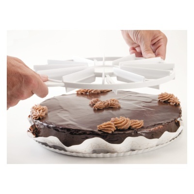 Bolo redondo com cobertura de chocolate e chantilly castanho, sendo separado em fatias com um utensílio plástico branco.