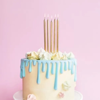 Bolo com cobertura branca e gotas azuis, cinco velas douradas acesas e suspiros no topo