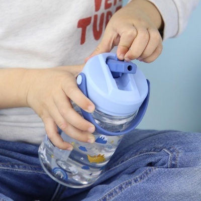 Garrafa de água azul com desenhos de dinossauros nas mãos de uma criança