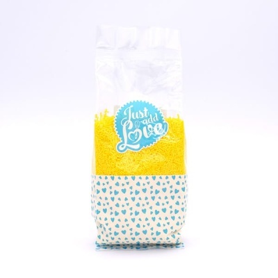 Embalagem transparente com produto amarelo, padrão azul de corações e rótulo 'Just add Love'