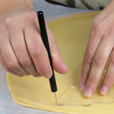 Mão usando ferramenta preta para cortar massa amarela com molde de coração transparente