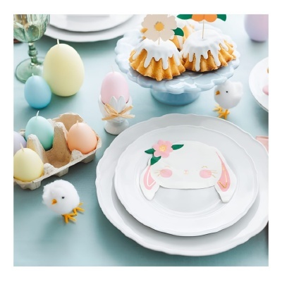 Mesa de Páscoa com pratos brancos e decoração de coelho, ovos coloridos e patos de pelúcia