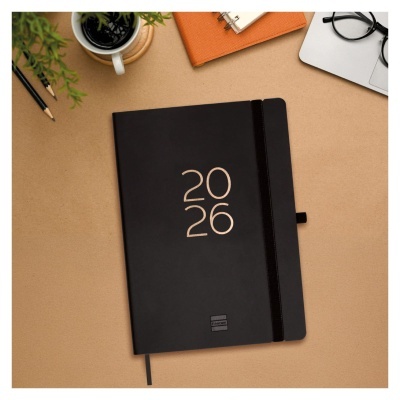 Agenda preta com 2026 na capa sobre mesa com acessórios