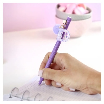 Caneta roxa com pendentes na mão a escrever num caderno quadriculado