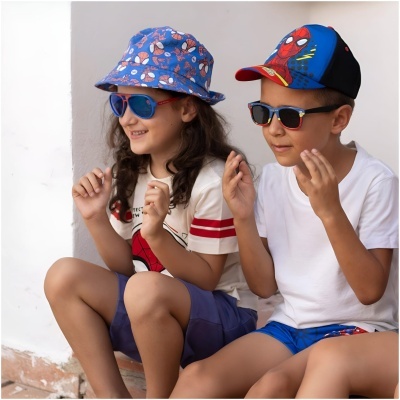 Duas crianças com chapéus e óculos escuros, vestindo roupas temáticas do Homem-Aranha, sentadas junto a uma parede branca.