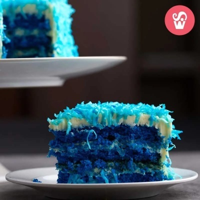 Fatia de bolo azul com cobertura branca e granulados azuis num prato branco