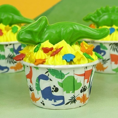 Cupcake com decoração de dinossauros coloridos e topper de dinossauro verde em forma de papel decorado com dinossauros.