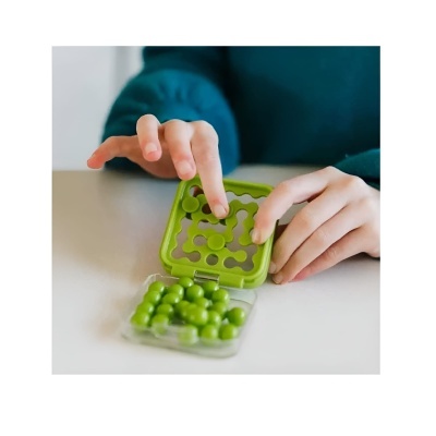 Puzzle de bolso verde com peças esféricas verdes e mãos infantis sobre mesa branca