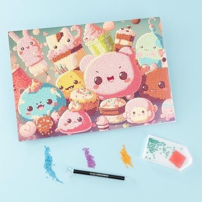 Quadro de doces coloridos kawaii feito com pedrinhas coloridas e ferramentas de aplicação sobre uma superfície clara.