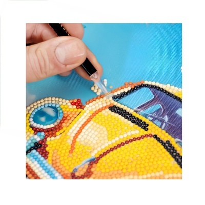 Detalhe de artesanato em miçangas coloridas formando um carro amarelo sobre tecido azul