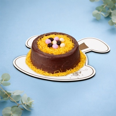 Bolo decorado com chocolate, fios amarelos e ovos de chocolate sobre base de coelho