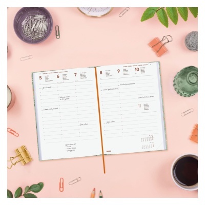 Calendário semanal aberto numa mesa rosa com material de escritório à volta