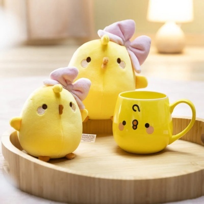 Dois bonecos de peluche amarelos com laços rosa e uma caneca amarela com rosto sorridente numa bandeja de madeira