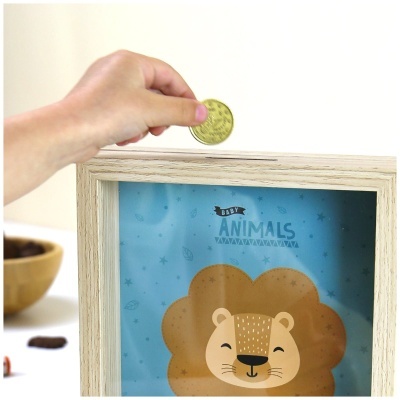 Mão a colocar moeda numa caixa de poupança de madeira com desenho de leão e texto BABY ANIMALS