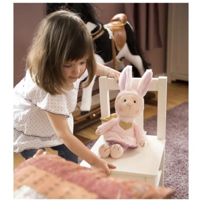 Criança com boneco de peluche rosa em cadeira branca e cavalo de baloiço ao fundo