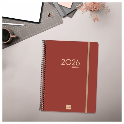 Agenda 2026 terracota com elástico castanho numa mesa cinza clara com acessórios de escritório