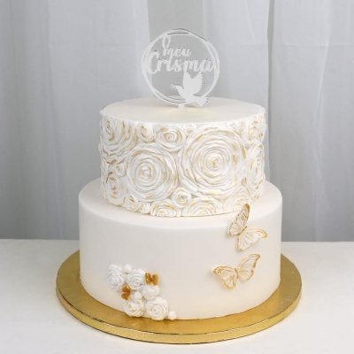 Bolo branco decorado com flores e borboletas douradas e topper com texto meu Crisma