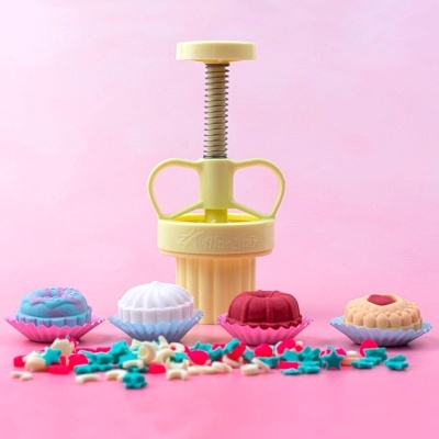 Extrusor amarelo para bolachas com bolachas coloridas em fundo rosa