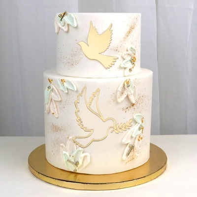 Bolo branco de dois andares com decoração de pombas douradas e flores em tons pastel.