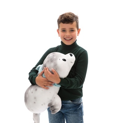 Menino com camisola verde e jeans segurando peluche de foca cinzenta