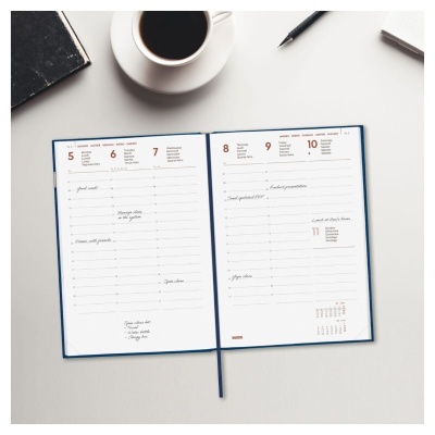 Agenda semanal aberta sobre mesa com caneca de café, caderno preto e caneta preta